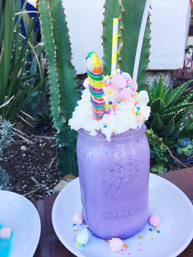 Unicorn milkshake in purple mason jar topped with whipped cream, sprinkles, lollipop and marshmallows. #unicornfoods #unicornmilkshake #unicorns #partyfood #unicornparty #unicorntreats #unicornpartytreats  livingmividaloca.com