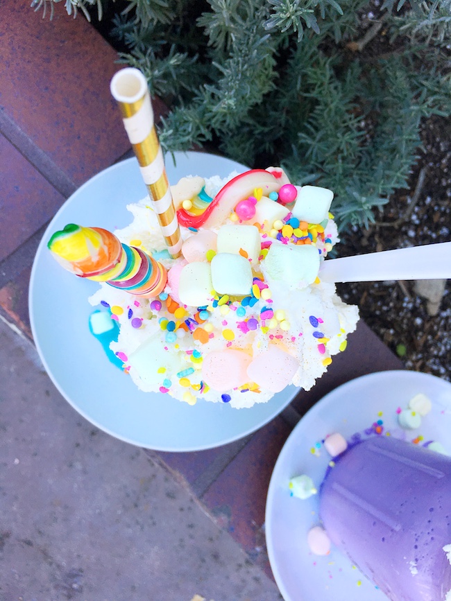 Unicorn milkshake in purple mason jar topped with whipped cream, sprinkles, lollipop and marshmallows. #unicornfoods #unicornmilkshake #unicorns #partyfood #unicornparty #unicorntreats #unicornpartytreats  livingmividaloca.com